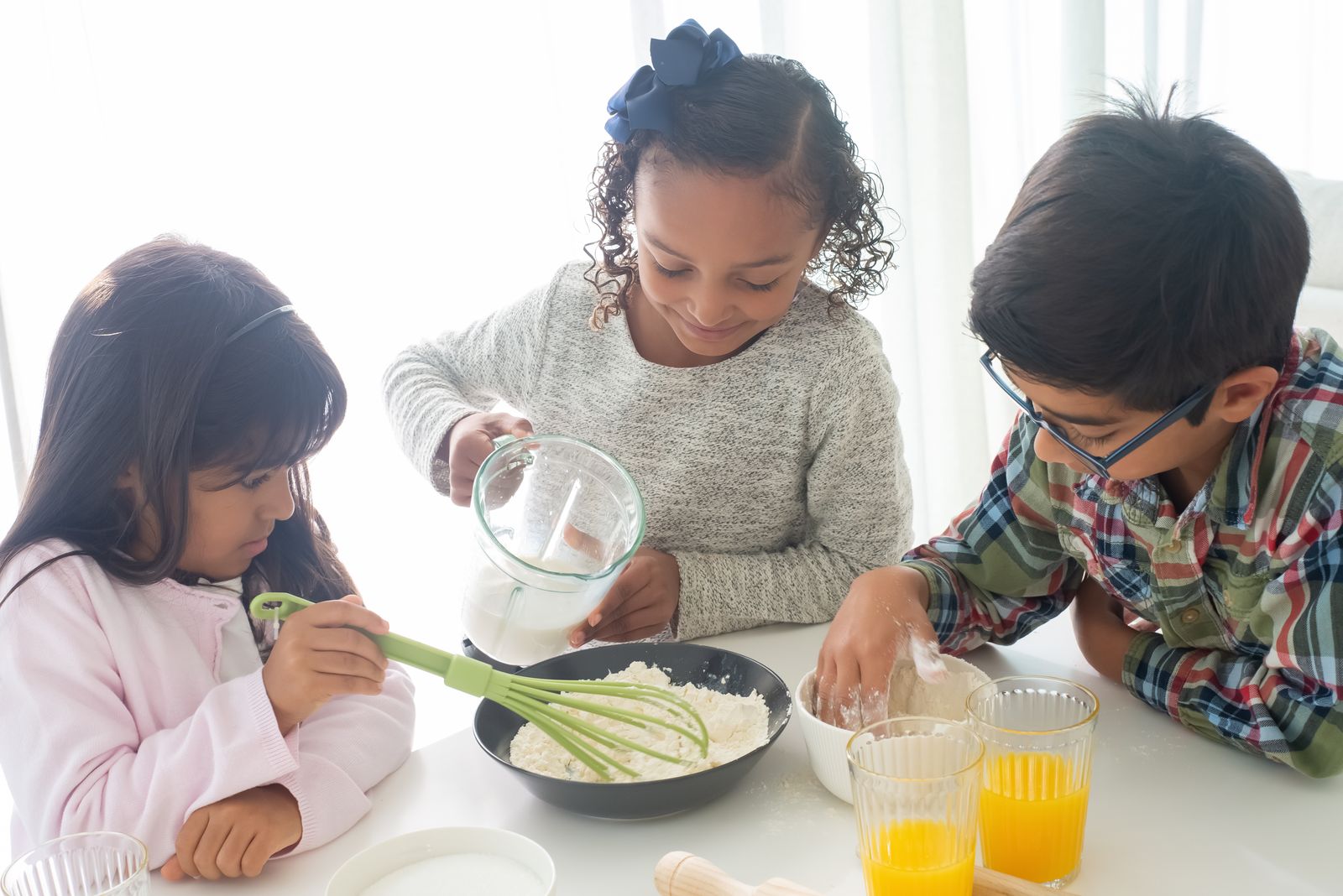 Three children mixing ingredients together in a bright kitchen