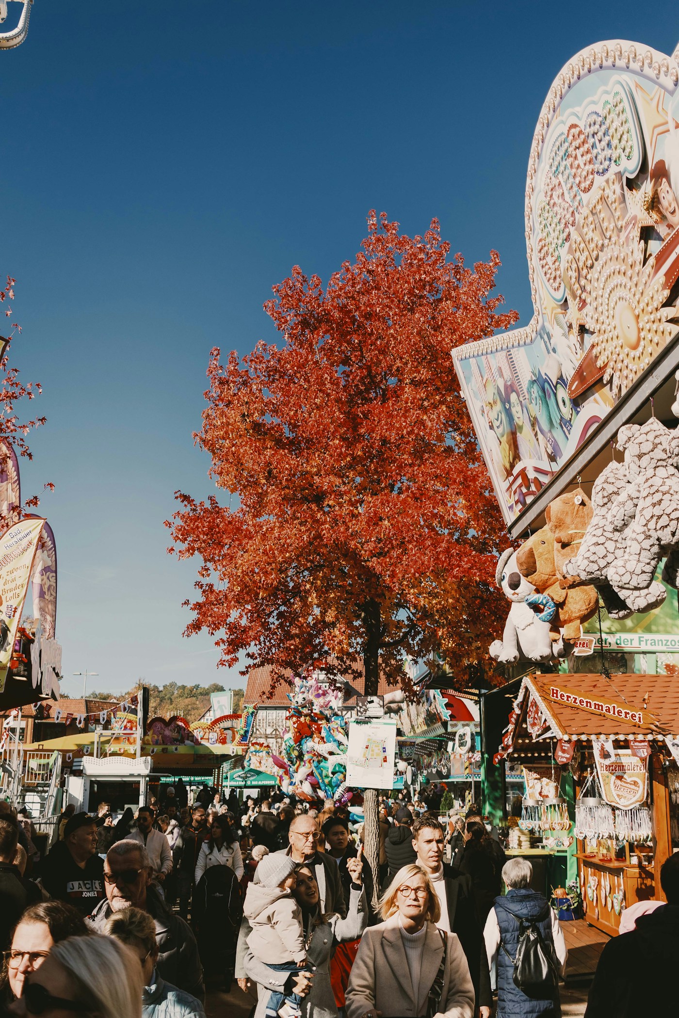 An outdoor fair beneath a bright orange autumn tree