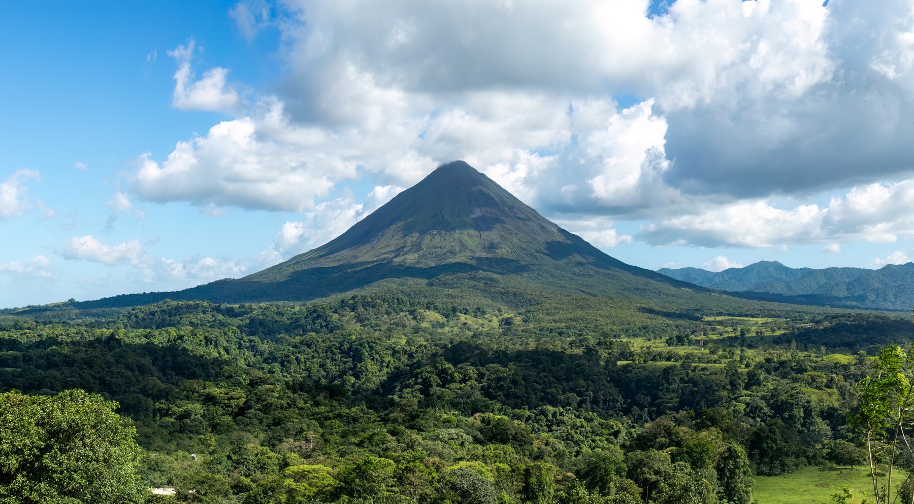 Arenal Volcano rising above lush green forest under a blue sky, Costa Rica