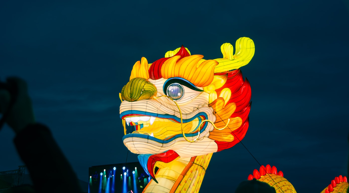 A brightly illuminated yellow and red dragon lantern against the evening sky