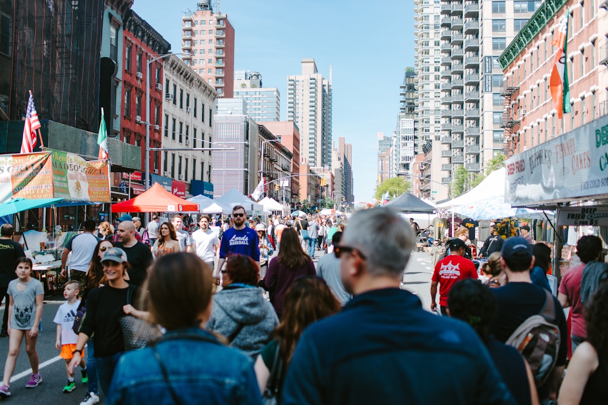 Families browsing food stalls at a sunny outdoor street fair